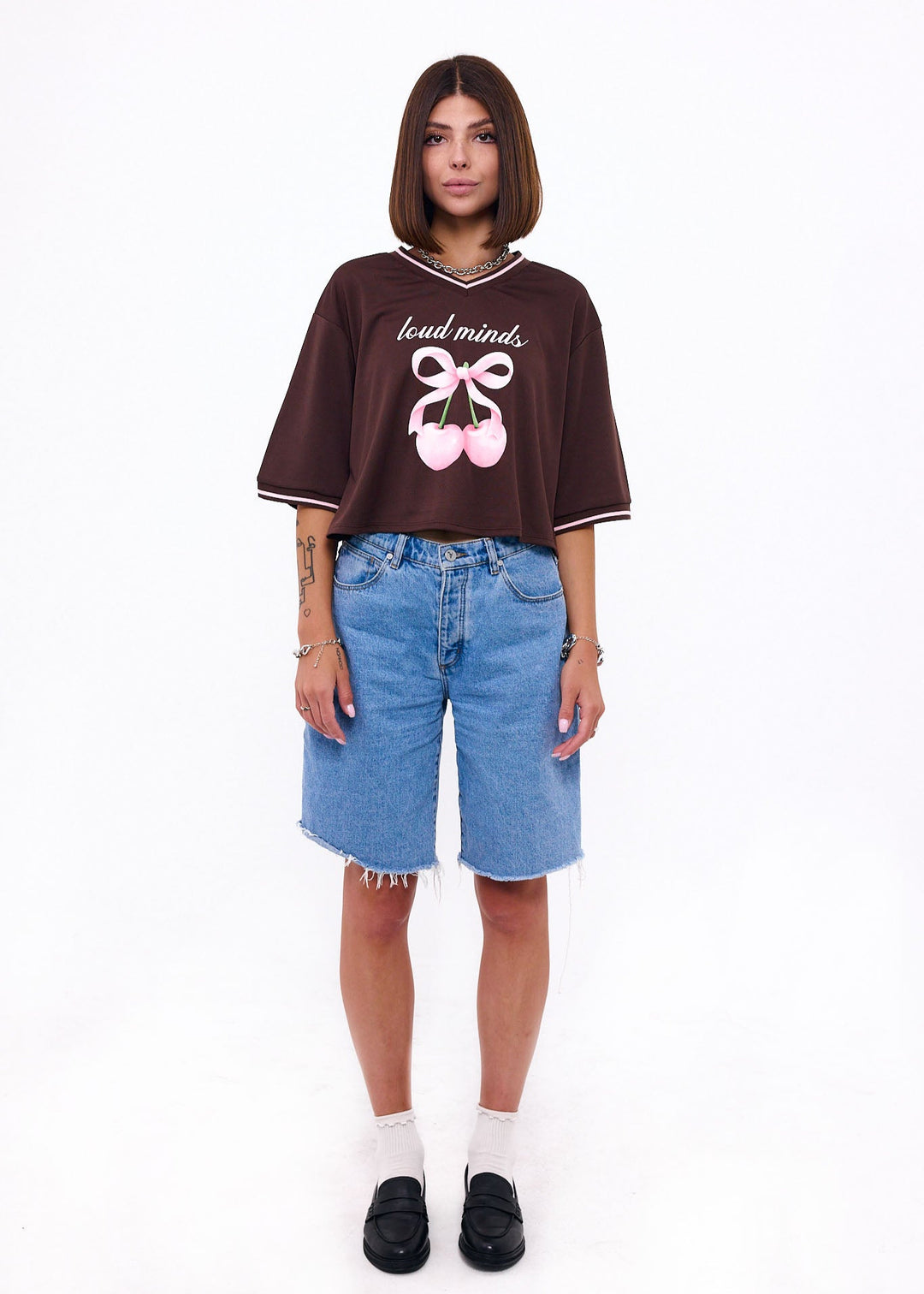 Person wearing a brown oversized t-shirt with text and graphics, paired with blue shorts on a white background