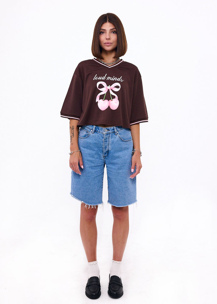 Person wearing a brown oversized t-shirt with text and graphics, paired with blue shorts on a white background