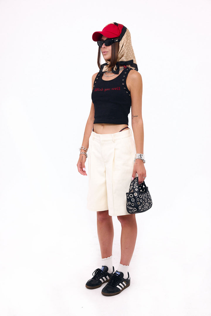 Person wearing a black tank top with red text, white shorts, black sneakers, and a red cap on a white background.