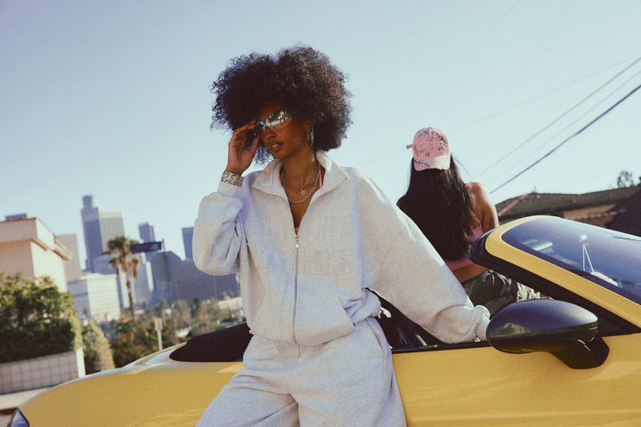 Person in a Heather Grey outfit sitting on a yellow car with a cityscape in the background
