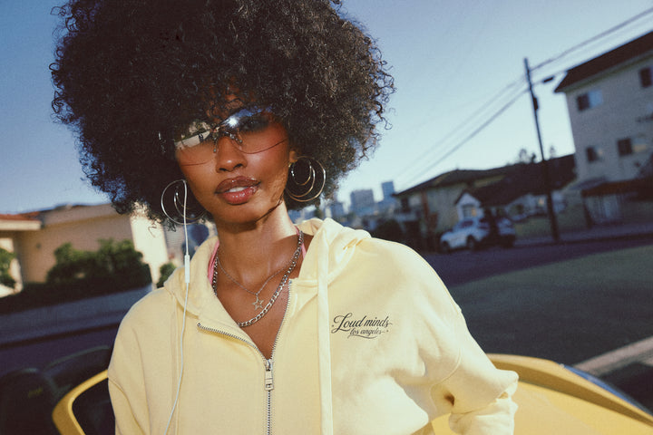 A woman with a large black afro hairstyle wearing a pale yellow zip-up hoodie with &